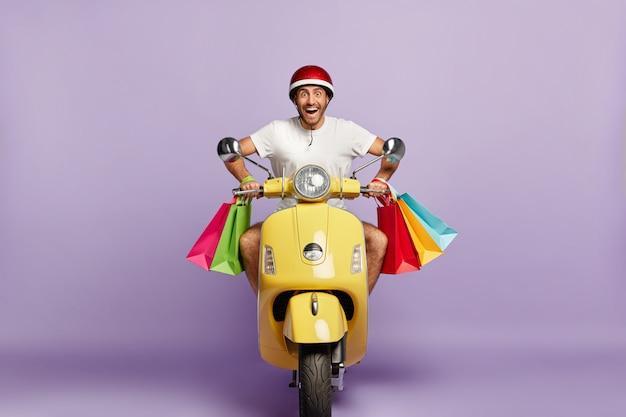 Веселый парень в шлеме и сумках за рулем желтого скутера